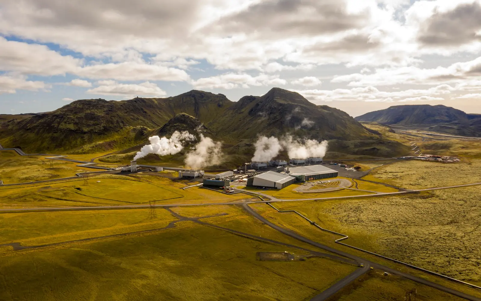 Geothermie: Erdsonde am Haus und tiefe Wärme fürs Netz sind zwei Projekte – Tiefe Geothermie: Erdwärme aus einem Geothermiekraftwerk Geothermiekraftwerk Hellisheiði mit Dampffahnen in einer isländischen Berglandschaft