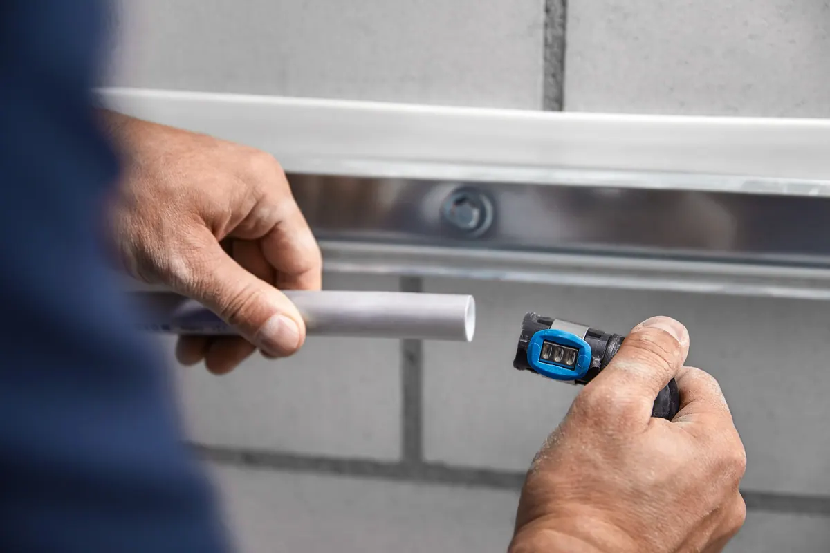 Ein Monteur steckt ein Rohr in ein Geberit FlowFit-Fitting mit blauem Pressindikator