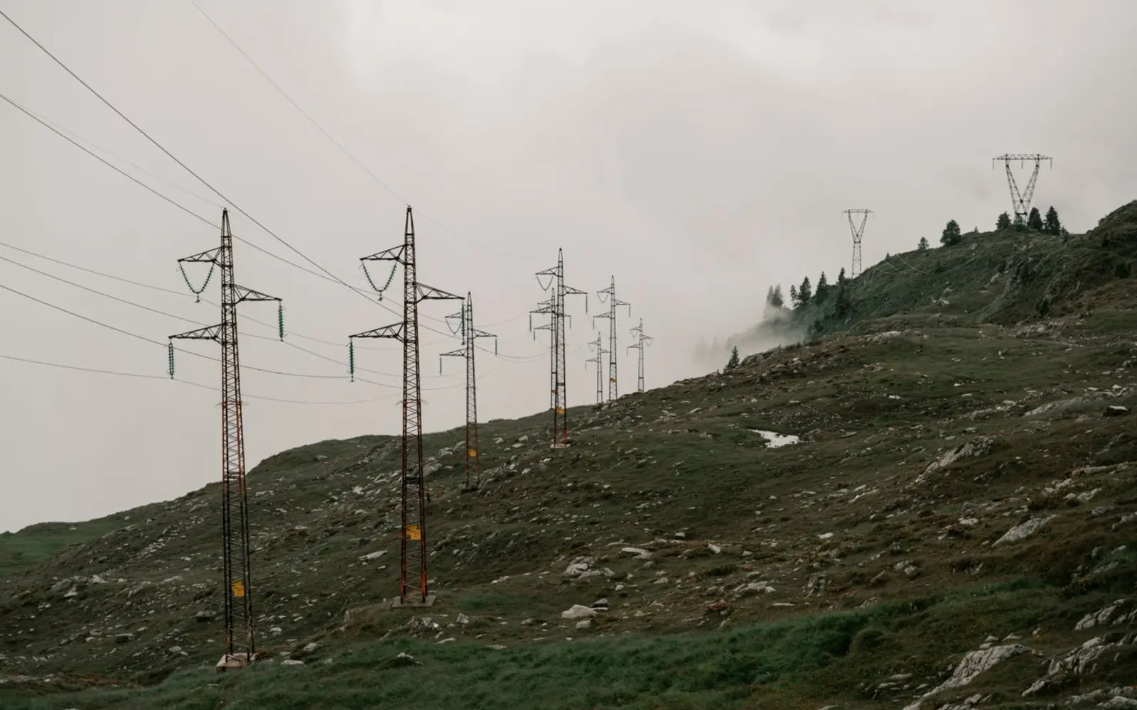 Schweiz 2027: Strompreise sinken – was bedeutet das für Wärmepumpen? – Schweiz 2027: Stromnetz in einer Berglandschaft Stromleitungen verlaufen über einen nebligen Berghang als Symbol für das Schweizer Stromnetz und regionale Tarife