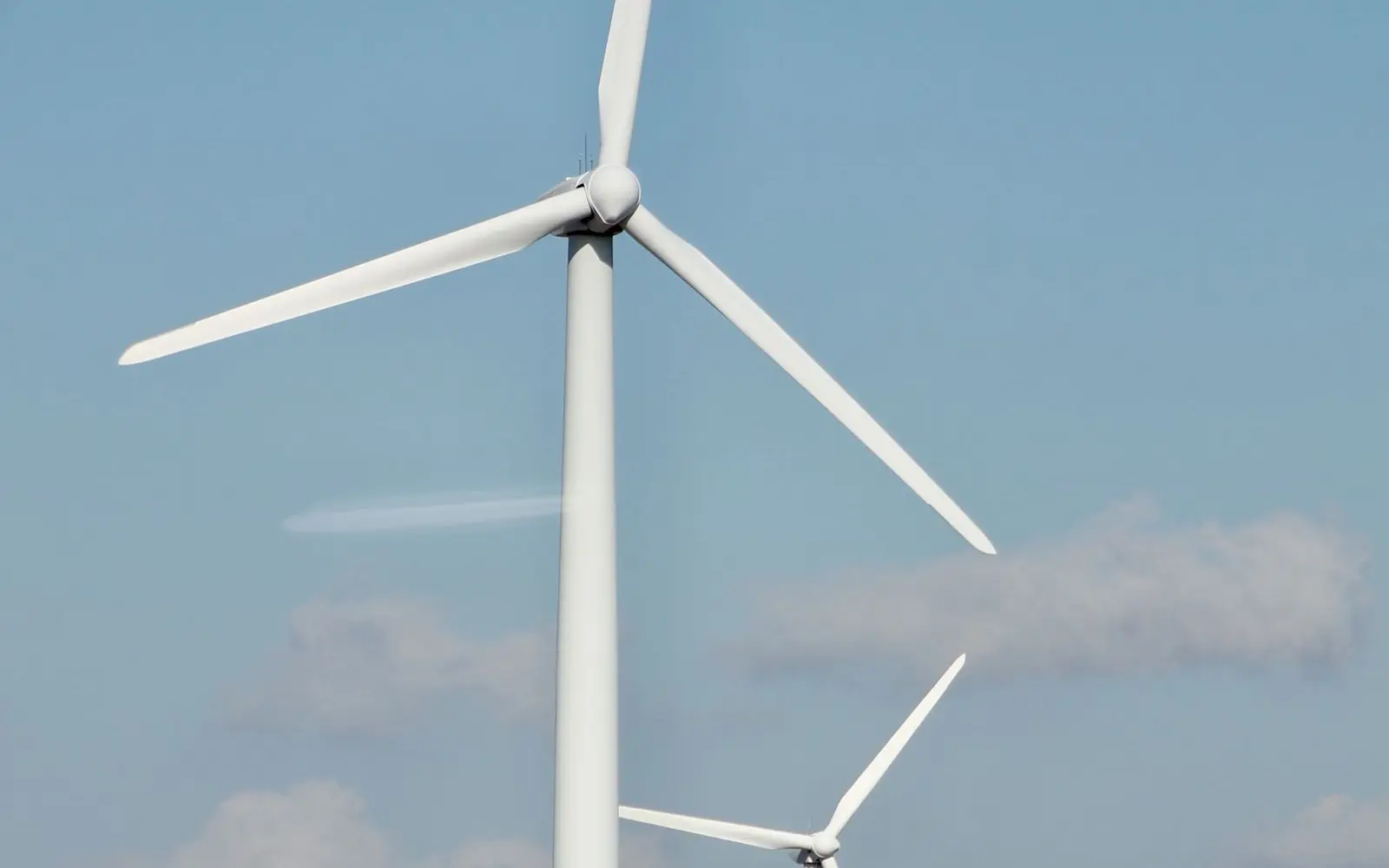 Weiße Windkraftanlagen vor blauem Himmel als Beispiel für Stromerzeugung aus Windenergie